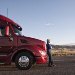 Truck driver leaning on the grill of his commercial truck.